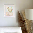 Load image into Gallery viewer, Querin Creations Framed watercolour artwork of a cactus on a wall with a lamp and decorative plant in the foreground above white sofa. Minimal, relaxing Home decor