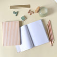 Load image into Gallery viewer, Open notebook with a yellow stripes notebook overlapped on a light desk with a candle and gold and green stationery items