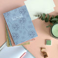 Load image into Gallery viewer, Floral notebook on a pink background desk surface with stationery items
