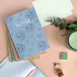 Floral notebook on a pink background desk surface with stationery items