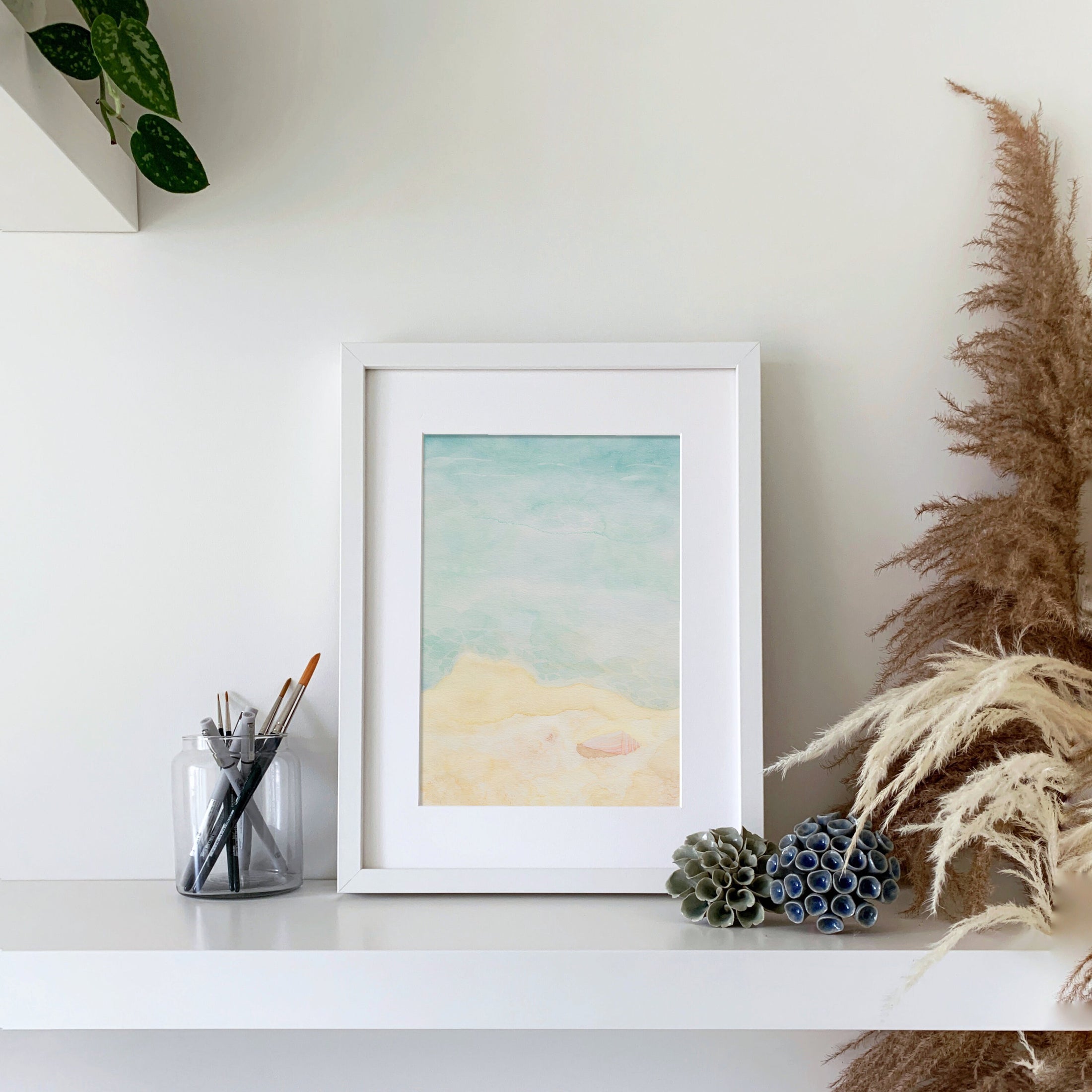 Querin Creations Watercolour seaside artwork on a shelf with decorative items and plants.