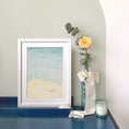 Load image into Gallery viewer, Querin Creations Framed contemporary watercolour artwork of a shell on a beach on a blue desk with a vase of flowers and a candle.
