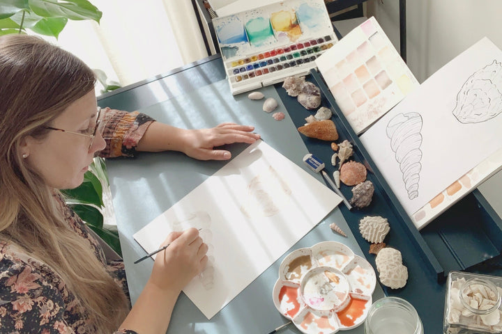 Giorgia painting in her studio with watercolours at a table with art supplies