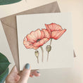 Load image into Gallery viewer, Querin Creations square greeting Card with pink poppy flowers held by a hand, with a brown craft envelope.
