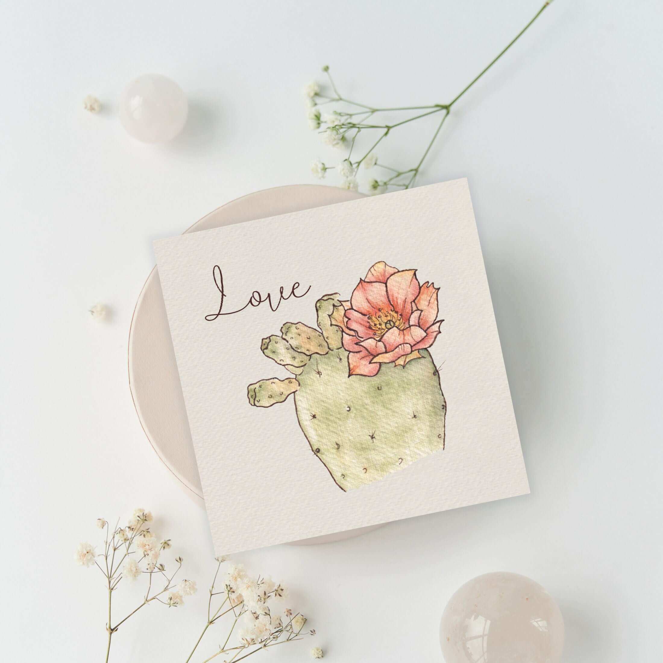 Querin Creations square greeting card with a cactus and flower illustration and the word 'Love' on a light background.