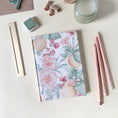 Load image into Gallery viewer, Floral notebook with stationery items on a light desk with a candle and relaxed atmosphere 
