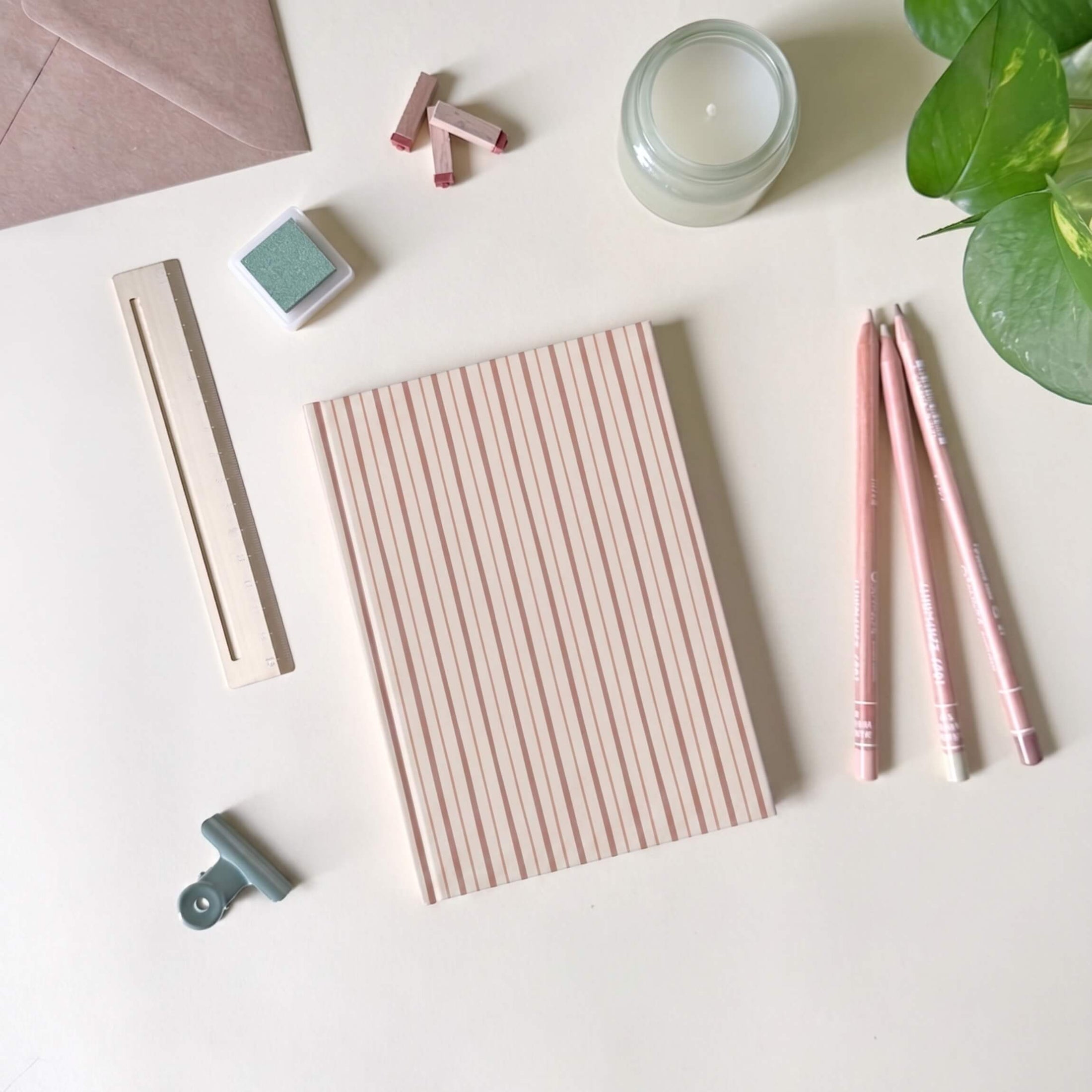Stationery items including a red striped notebook, pens, and a candle on a light surface.
