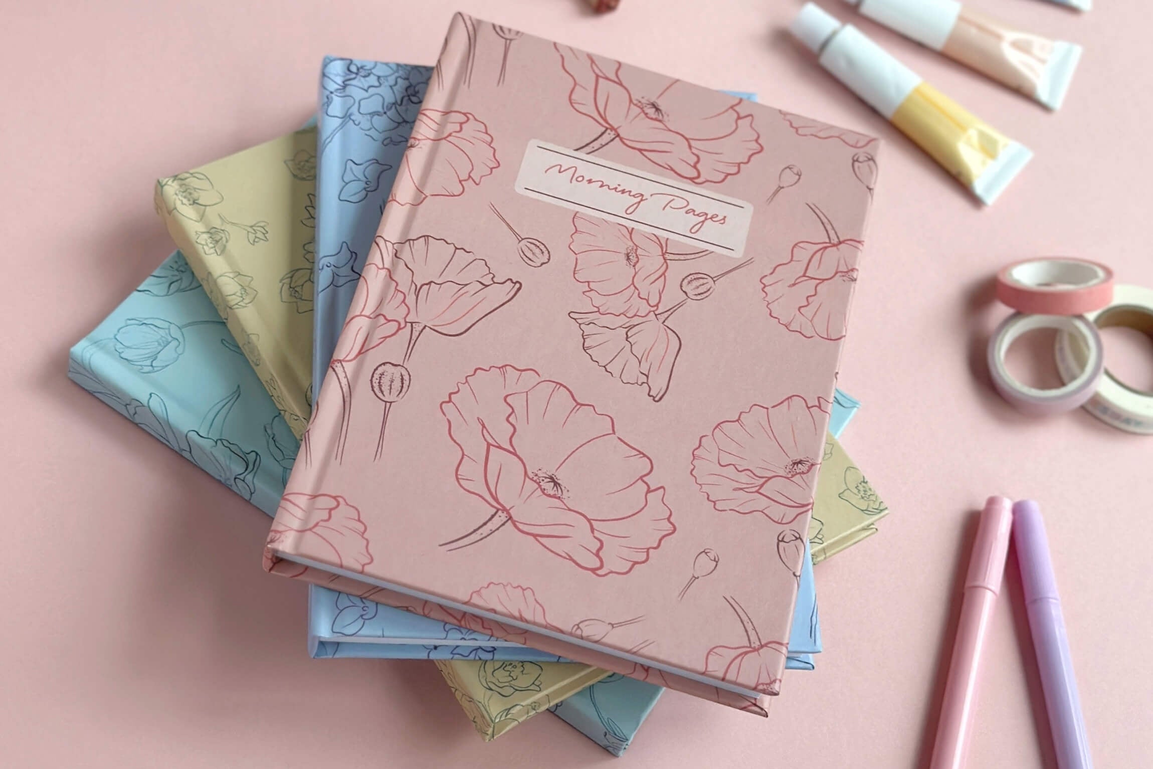 Stack of floral notebooks on a pink background with stationery items.